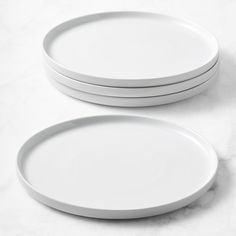 three white plates sitting next to each other on a marble counter top with one empty plate in the middle