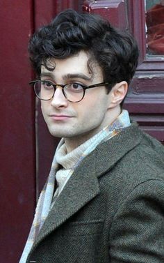 a young man wearing glasses standing in front of a red door and looking at the camera