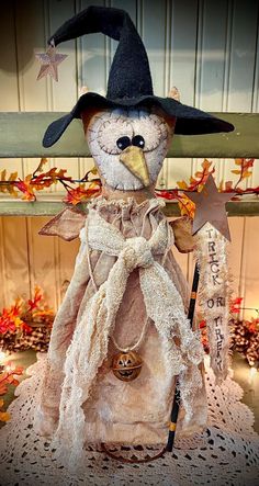 a stuffed snowman wearing a witches hat and holding a broom on top of a doily