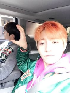 two young men sitting in the back seat of a car, one with red hair