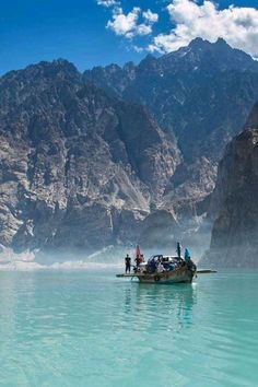 people on a boat in the middle of a lake with mountains in the background and blue water