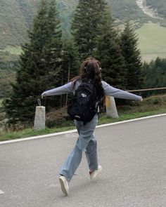 a woman walking down the road with her arms spread out and trees in the background