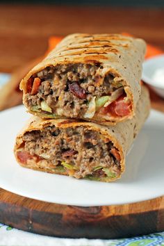 two burritos sitting on top of a white plate next to a wooden cutting board