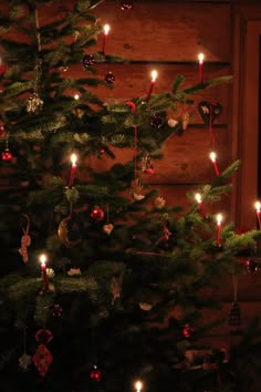 a christmas tree with lit candles and ornaments hanging from it's branches in front of a wooden wall