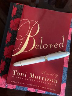 a pen sitting on top of a red book with the title beloved written in gold