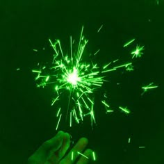 a hand is holding a green sparkler in the dark