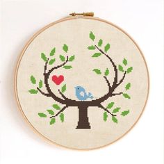 a cross stitch pattern with a blue bird sitting on a tree and heart in the branches