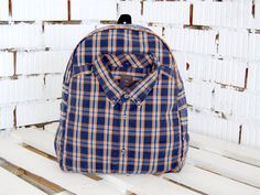 a blue and yellow plaid backpack sitting on top of a wooden bench in front of a white brick wall