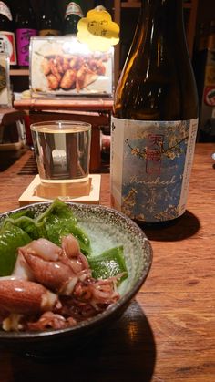 a bowl of food next to a bottle of wine on a table with other items