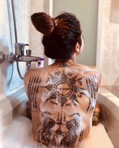 a woman with tattoos on her back sitting in a bathtub