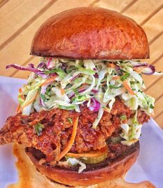 a sandwich with meat, coleslaw and lettuce on a bun sitting on a plate