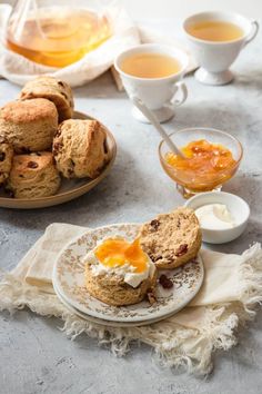 scones with butter and jam are on the table next to cups of tea or coffee