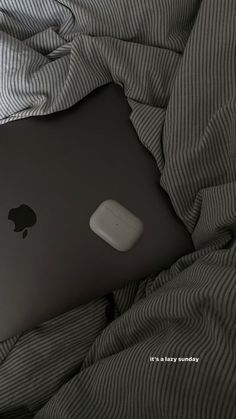 an apple laptop computer sitting on top of a bed covered in gray and white sheets