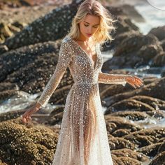 a woman in a long dress standing on rocks by the ocean with her arms outstretched