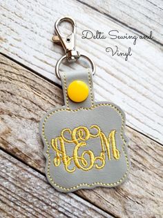 a gray and yellow keychain with an embroidered monogramm on it