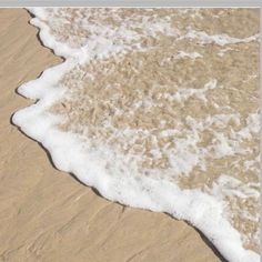 an ocean wave rolls in on the sand at the edge of the beach, with a surfboard sticking out of the water