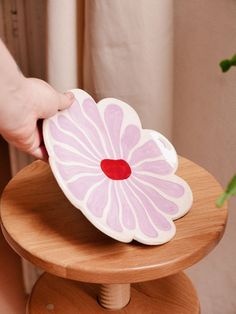 a person holding a pink flower shaped object on top of a wooden stool