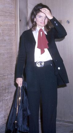 a woman in a suit and red tie holding a handbag while standing next to a door