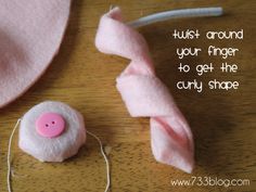 a pink hat with a pink button on it next to a sewing needle and thread