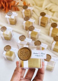 a person holding up some gold and white wedding favors in front of a table full of coins