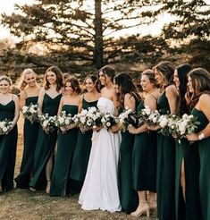 a group of women standing next to each other in front of trees and grass holding bouquets