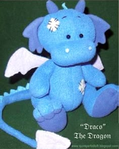 a blue dragon stuffed animal sitting on top of a green surface with the caption draco the dragon