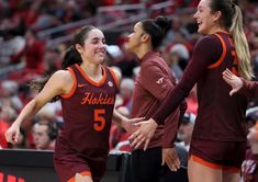 three women in maroon and orange uniforms standing on a court with their arms around each other