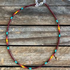 a colorful beaded necklace is sitting on a wooden surface with a silver chain around it