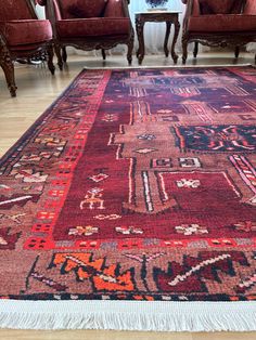 a red rug with an intricate design on the floor in a living room next to two chairs