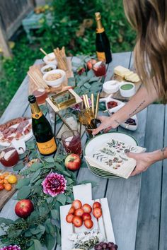 a table full of food and drinks on top of a wooden picnic table with bottles of wine