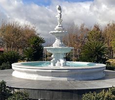 there is a white fountain in the middle of a park with trees and bushes around it