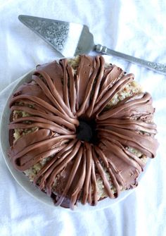 a chocolate frosted cake on a white plate with a knife and fork next to it