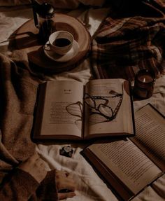 an open book sitting on top of a bed next to two glasses and a cup