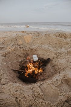 an open fire pit on the beach with water in the background and sand around it