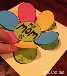 a person holding up a flower shaped card with the word mom on it's side