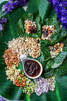 an assortment of food on a plate with purple flowers in the background and green leaves surrounding it