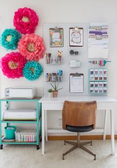 a white desk topped with lots of pink and blue flowers next to a wall mounted bulletin board