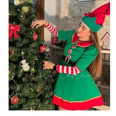 a woman dressed in green and red decorating a christmas tree