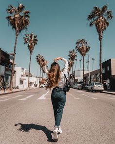 a woman is walking down the street with her hair in the air and palm trees behind her