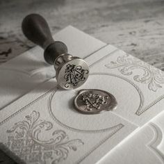 a stamper is sitting on top of an ornate white envelope with a monogrammed seal