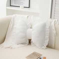 a white pillow with ruffles on it sitting on a couch next to a book