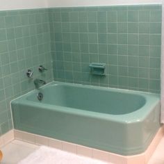 a bath tub sitting next to a toilet in a bathroom with green tiles on the walls