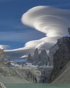 some very pretty clouds in the sky over mountains and water with snow on it's sides