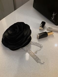 a black rose, lipstick, and other makeup items on a counter top next to a bag