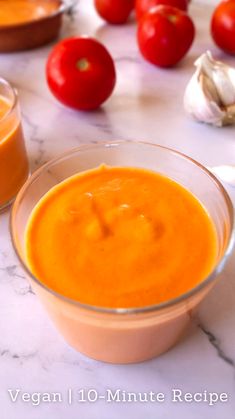 there is a bowl of soup on the table with some tomatoes and garlic around it