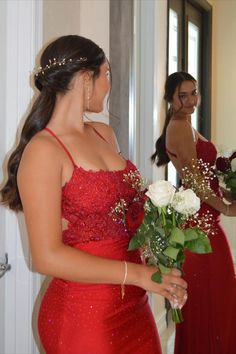 a woman in a red dress is holding flowers and looking at herself in the mirror