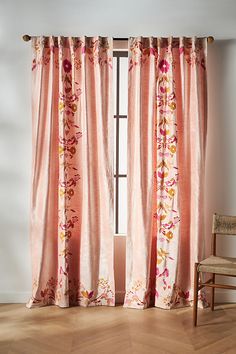 a chair sitting next to a window covered in pink curtains