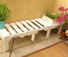 a white bench sitting on top of a wooden floor next to potted planters