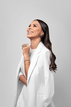 a woman in a white suit smiling and holding her hand up to her face,