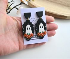 a pair of black and white penguin earrings with orange flowers on the bottom, hanging from a card